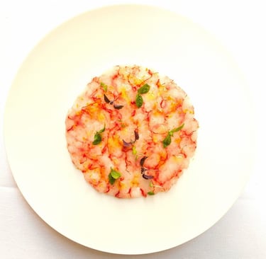 Un plato blanco con un carpaccio de gambas en forma circular