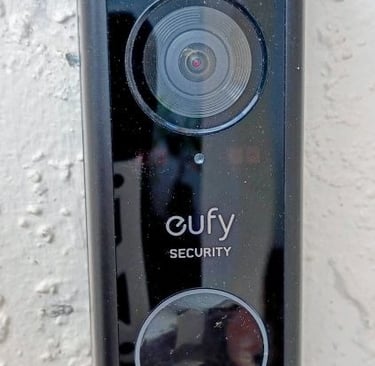 Black Eufy security camera and doorbell mounted on home white vexterior wall