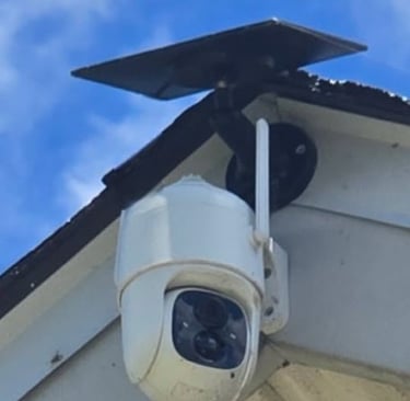 Solar powered wireless outdoor security camera mounted on a house roof against a blue sky.