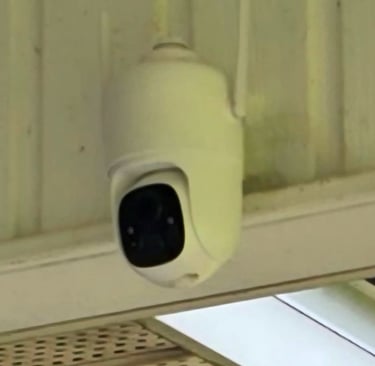 A white outdoor smart security camera with dual antennas mounted under a roof for home surveillance.