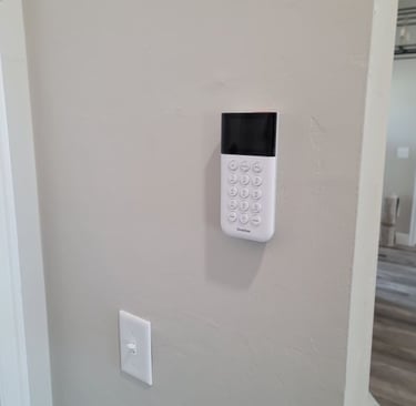 White SimpliSafe home security system keypad mounted on a neutral wall near a light switch.