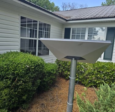 A rectangular Starlink satellite internet dish mounted on a pole outside a residential white house.