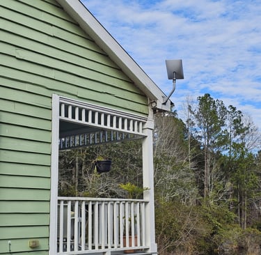 A Starlink satellite dish mounted on the roof of a green house with a white porch railing.