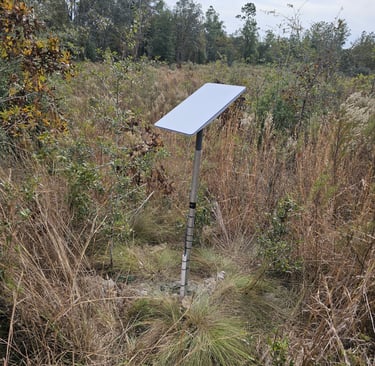 A Starlink satellite dish mounted on a pole in a rural field for remote internet access.