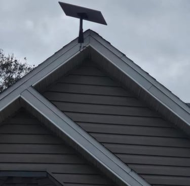 A Starlink satellite internet dish mounted on the peak of a residential roof against a cloudy sky.