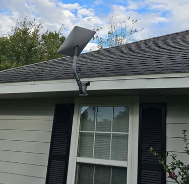 A Starlink satellite internet dish mounted on a residential house roof under a cloudy blue sky.