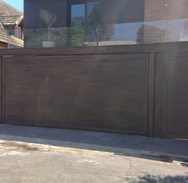 Vista aproximada do portão de garagem basculante e do portão social com acabamento em pintura que imita o aço corten, em fren