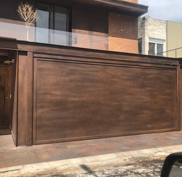 Portão de garagem basculante de alumínio com acabamento em pintura especial na cor bronze, em frente a uma casa de tijolinhos
