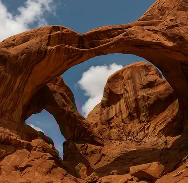 Low-angle view of Double Arch in Arches National Park, showcasing two massive red rock arches against a bright blue sky with 