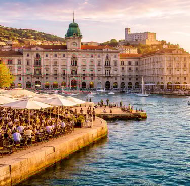 Trieste’s Piazza Unità d’Italia waterfront at golden hour, elegant historic buildings, café umbrellas, and Adriatic Sea views