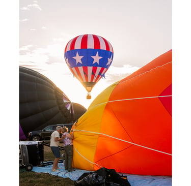 A colorful hot air balloon festival at sunrise with people preparing large balloons for flight.