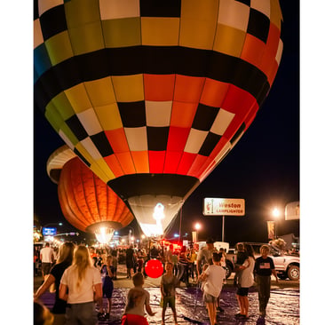 Colorful checkered hot air balloons glowing at night during a crowded summer festival event.