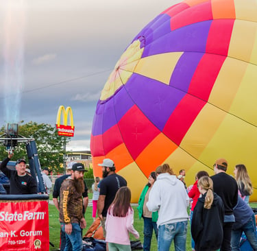 A colorful hot air balloon being inflated with a gas burner flame at an outdoor festival.