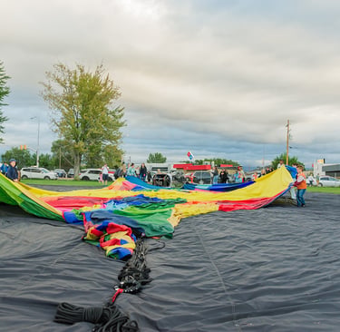 People preparing a colorful hot air balloon envelope for inflation in an outdoor grassy field.