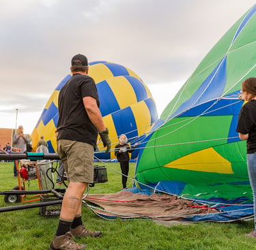 Ground crew members preparing a colorful green and blue hot air balloon for launch on a grassy field.