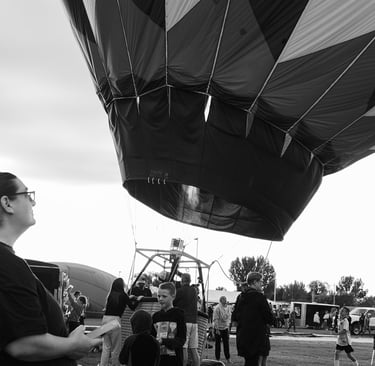 Black and white image of woman watching large hot air balloon is inflated and prepared for flight at an outdoor festival.