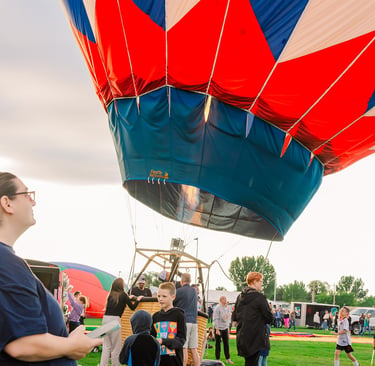 A colorful red, white, and blue hot air balloon being prepared for flight at an outdoor festival.