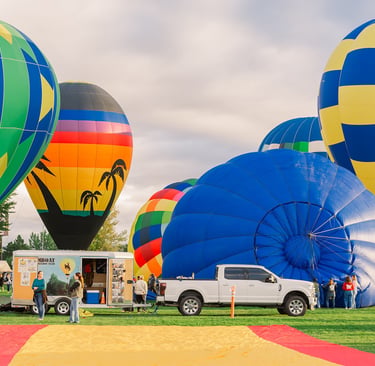 Colorful hot air balloons inflating at an outdoor festival with spectators and a white pickup truck.