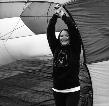 A smiling woman in a black hoodie holding open a large hot air balloon envelope during setup.