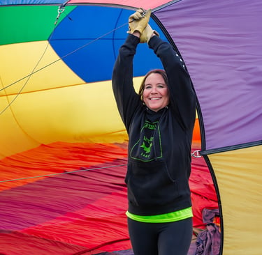 A woman holds open a colorful rainbow hot air balloon envelope during inflation.