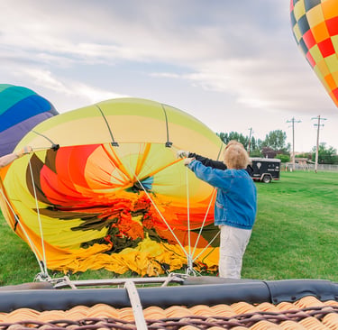 Ground crew inflating a colorful hot air balloon envelope on a grassy field during a festival.