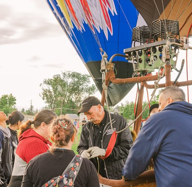 A hot air balloon pilot demonstrates burner equipment to a group of people at a balloon festival.