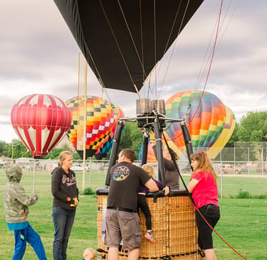 A group of people prepares a hot air balloon for flight in a grassy field during a colorful balloon festival.