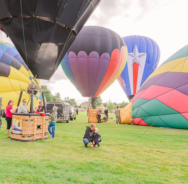 Colorful hot air balloons preparing for takeoff on a green grass field during a festival.