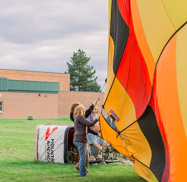 A ground crew prepares a colorful hot air balloon for inflation on a grassy field.