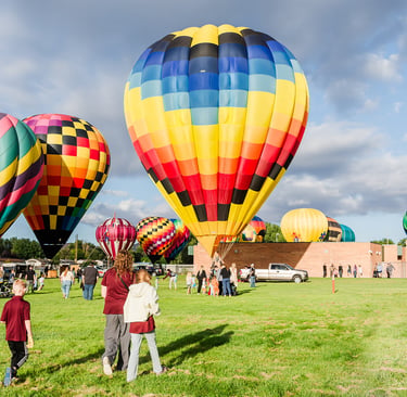 Colorful hot air balloons taking off from a green field at a summer festival with spectators.