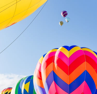 Colorful hot air balloons with chevron patterns floating in a clear blue sky during a festival.