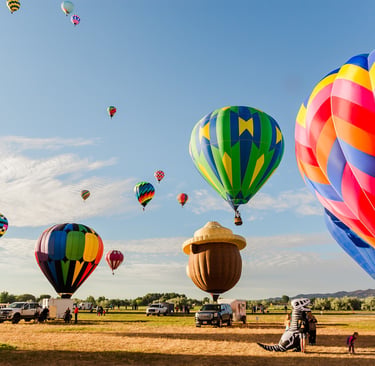 Colorful hot air balloons taking off from a field during a morning festival under a clear blue sky.