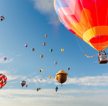 Colorful hot air balloons and a unique acorn balloon floating in a clear blue sky during a festival.