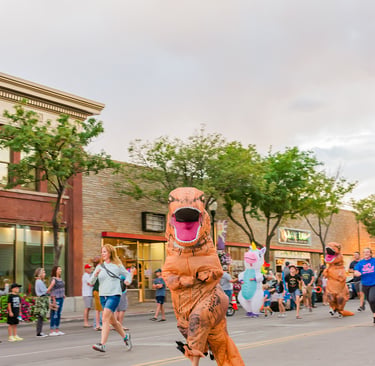 A group of people running down a city street in inflatable T-Rex dinosaur costumes during a fun run event.