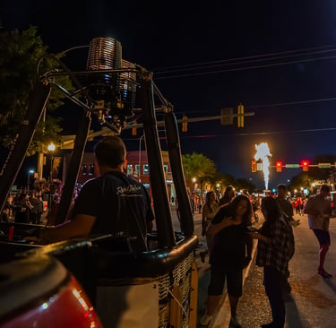 Hot air balloon burner glowing at a night festival with crowds on a city street.