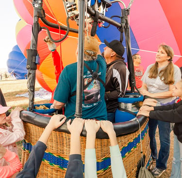 Excited family and crew preparing a colorful hot air balloon for flight with a wicker basket.