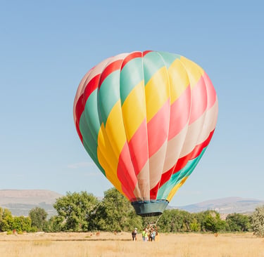 Colorful hot air balloon taking off from a golden field with mountains in the background.