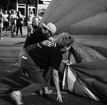 A black and white photo of people preparing a hot air balloon for inflation at an outdoor festival.
