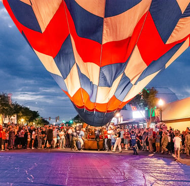 A colorful hot air balloon inflating over a crowded city street during a festive evening event.