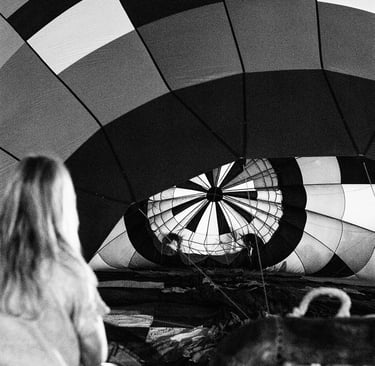 Black and white photo of a person watching a checkered hot air balloon being inflated.