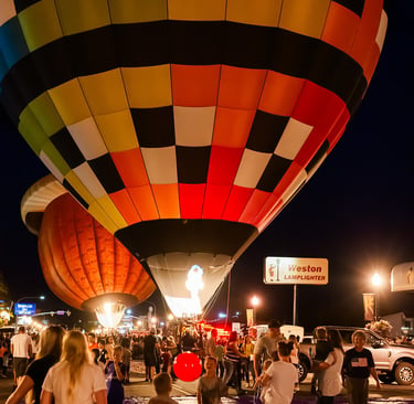 Crowd watching colorful hot air balloons glowing at night during a festival glow event.