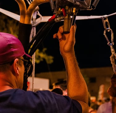 A hot air balloon pilot operates the propane burner system during a night glow event.