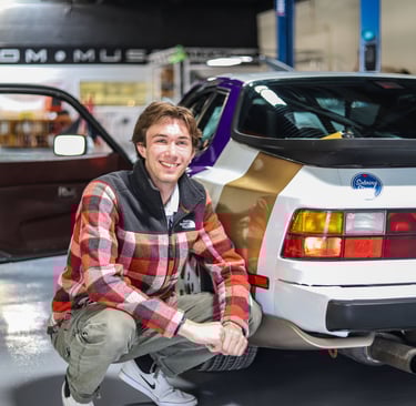 Luke Gilmore sitting next to a Porsche 944.
