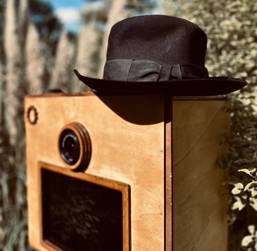 Détail du photobooth en bois vintage avec objectif apparent et chapeau posé, mise en scène poétique