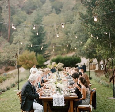 Dîner en plein air sous guirlandes lumineuses dans un jardin, longue tablée conviviale décorée 