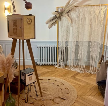Photobooth en bois artisanal installé dans une scénographie bohème avec macramé, tapis et éclairage