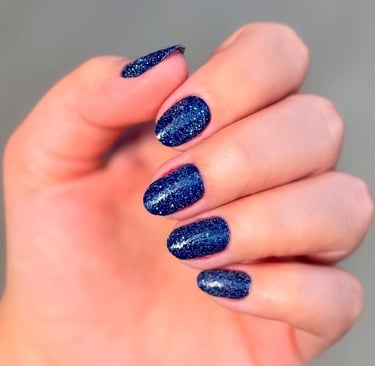 Esmaltação em gel azul marinho profundo com partículas de glitter prateado, apresentando brilho intenso e duradouro.