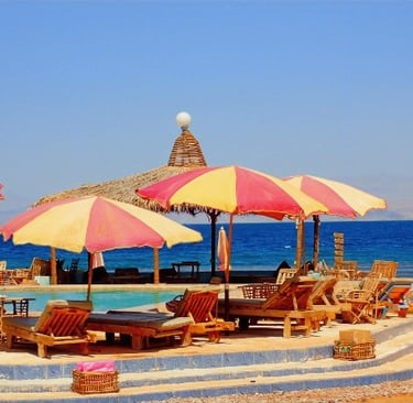 ein Strand in Ägypten mit Swimmingpool mit Meerblick und mit Sonnenschirmen und Stühlen