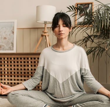 A woman practicing mindful meditation in a lotus pose during a home yoga session.