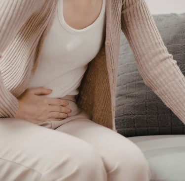 Woman sitting at home holding her stomach, feeling bloated and uncomfortable, representing digestive
